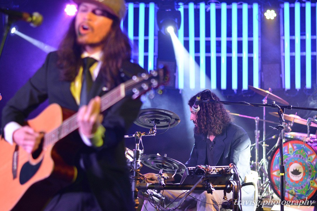 Drummer on a stage lit in blue, guitarist blurred in the foreground